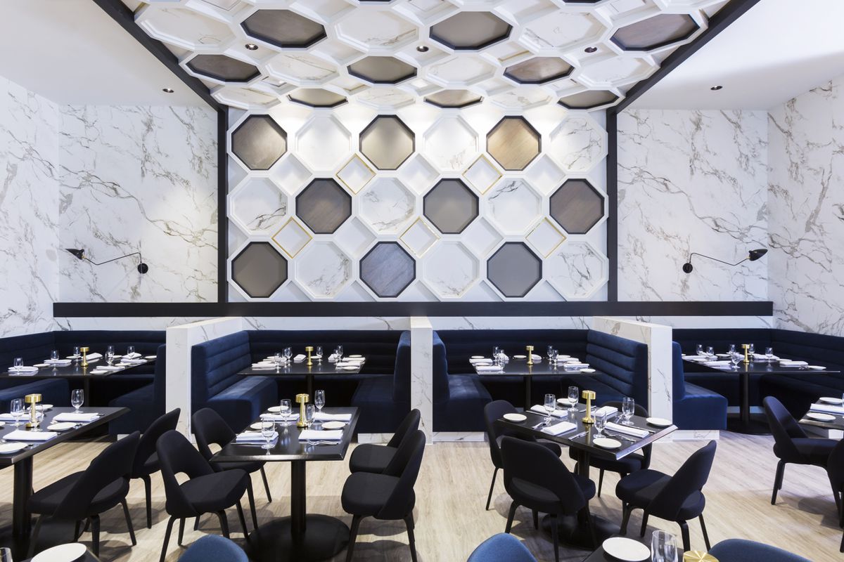  A restaurant dining room with blue velvet banquettes and a marble wall with an octagonal pattern.
