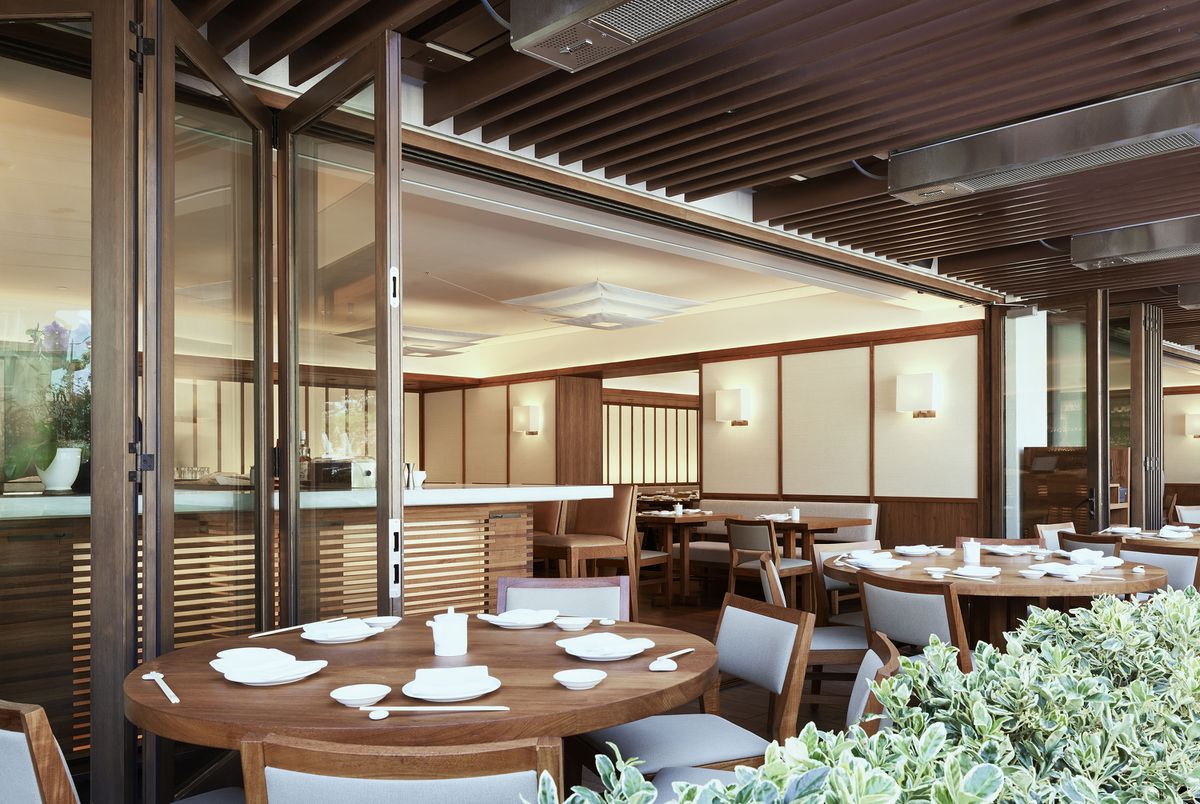  A restaurant dining room inspired by traditional Japanese design, with an open glass paneled accordion door separating an outdoor area from an indoor dining area.